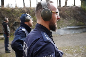 na zdjęciu widać stojących obok siebie policjantów, z nałożonymi na uszy słuchawkami ochronnymi