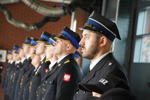 stojący w rzędzie strażacy podczas uroczystości. Wszyscy w mundurach galowych