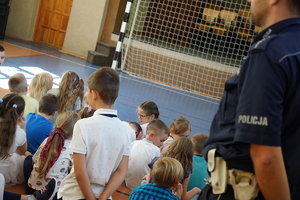 dzieci zgromadzone na sali gimnastycznej, po prawej stronie stoi policjant