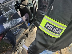 policjant zamyka drzwi radiowozu nieoznakowanego, w którym siedzi zatrzymany