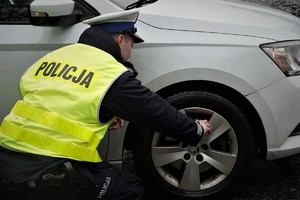 policjant drogówki kuca przy kole samochodu