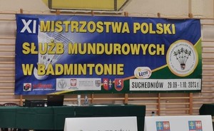 zdjęcie przedstawia baner XI Mistrzostw Policji Służb Mundurowych w Badmintonie. Na banerze znajdują się loga sponsorów oraz herb gminy Suchedniów.