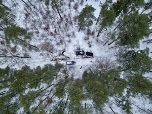 zdjęcie przedstawia trzy pojazdy i radiowóz w lesie. Widok z góry, z powietrza.