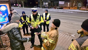 zdjęcie przedstawia policjantów, strażaków i strażników miejskich rozdających odblaski przechodniom