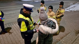 zdjęcie przedstawia policjantów, strażaków i strażników miejskich rozdających odblaski przechodniom