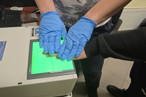 zdjęcie przedstawia zatrzymanego w trakcie pobierania odcisków linii papilarnych przez technika