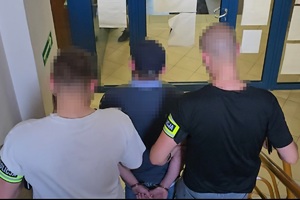 zdjęcie przedstawia zatrzymanego prowadzonego przez nieumundurowanych policjantów.