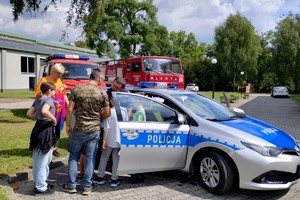 zdjęcie przedstawia policjanta prezentującego radiowóz uczestnikom pikniku