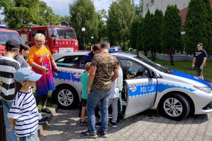 zdjęcie przedstawia policjanta prezentującego radiowóz uczestnikom pikniku