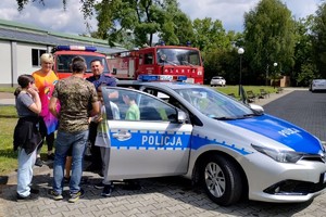 zdjęcie przedstawia policjanta prezentującego radiowóz uczestnikom pikniku