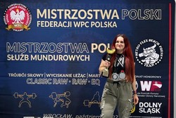 zdjęcie przedstawia policjantkę w stroju sportowym z pucharem i medalami na szyi