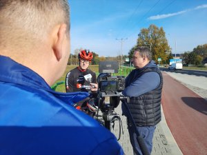 Kolarz na rowerze rozmawia z mężczyzną przed kamerą