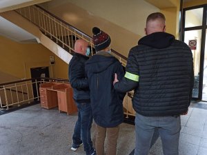Dwóch nieumundurowanych policjantów prowadzących podejrzanego w budynku Komendy Miejskiej Policji w Piekarach Śląskich