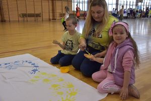 Przedstawicielka stowarzyszenia maluje z dziećmi serce w barwach niebiesko-żółtych