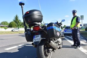Policjant ruchu drogowego stoi przy policyjnym motocyklu oraz radiowozie