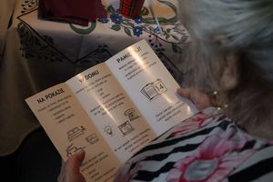 Zdjęcie przedstawia kobietę czytającą broszurę informacyjną dotyczącą oszustw