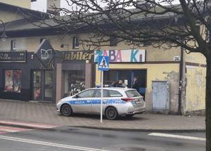 Zdjęcie policyjnego radiowozu oraz policjantów pomagających kobiecie