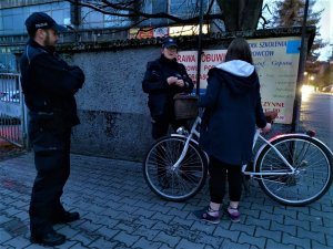 Zdjęcie kolorowe: umundurowani policjanci stoją obok młodej kobiety, która trzyma rower i rozmawia z policjantką