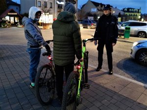 Zdjęcie kolorowe: dwóch nastolatków z rowerami stoi naprzeciwko policjantki