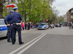 Zdjęcie kolorowe: dwóch umundurowanych policjantów z ruchu drogowego obserwuje ustawiającą się kolumnę motocyklistów