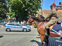 Zdjęcie kolorowe: z prawej strony widoczny patrol konny, z lewej oznakowany radiowóz policyjny.