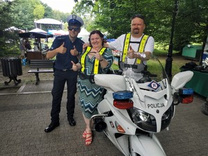 Zdjęcie kolorowe: umundurowany policjant ruchu drogowego z kobietą i mężczyzną przy policyjnym motocyklu pozują do zdjęcia.
