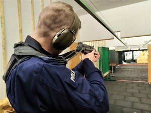 Zdjęcie przedstawia umundurowanego policjanta, który strzela z broni maszynowej stojąc.