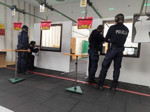 Zdjęcie przedstawia umundurowanych policjantów podczas ćwiczeń zza przesłony na strzelnicy.