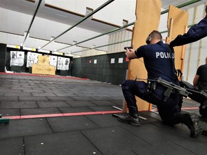 Zdjęcie przedstawia policjanta, który klęczy na jednym kolanie i wykonuje strzelanie do tarczy z broni krótkiej.