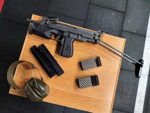 Zdjęcie przedstawia na stoliku broń maszynową, magazynki, amunicję i ochronniki słuchu.