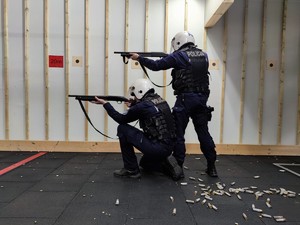 Zdjęcie przedstawia dwóch policjantów podczas strzelania z broni długiej. Jeden policjant klęczy, drugi stoi nad nim.