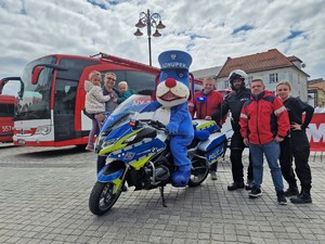 Zdjęcie przedstawia: policyjną maskotkę na motocyklu, mundurowych, uczestników Motoserca, a wśród nich dorośli i dzieci.