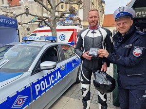 Zdjęcie przedstawia: policjanta, który wręcza apteczkę mężczyźnie w stroju motocyklowym.