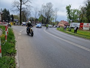 Zdjęcie przedstawia: motocykle jadące w paradzie. Z tyłu widoczny radiowóz i policjant blokujący drogę.