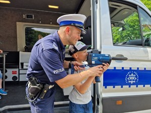 Zdjęcie przedstawia: umundurowanego policjanta oraz chłopca którzy trzymają przyrząd pomiaru prędkości