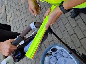 Zdjęcie przedstawia: rączkę wózka dziecięcego z zapiętą opaską odblaskową.