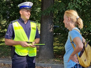 Zdjęcie przedstawia: uśmiechniętego policjanta podczas rozmowy z kobietą.