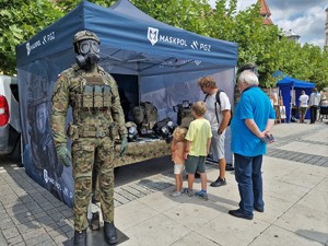 Zdjęcie przedstawia uczestników wydarzenia przy namiocie ze sprzętem wojskowym.