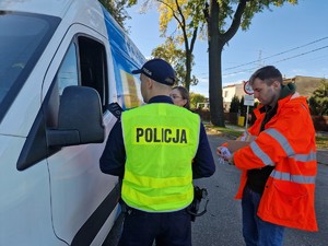 Zdjęcie przedstawia: 
Kierowcę samochodu dostawczego otrzymującego od przedstawiciela Kolei Śląskich ulotkę. Widoczny umundurowany policjant.