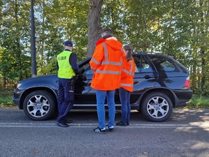 Zdjęcie przedstawia: 
Umundurowanego policjanta odbywającego rozmowę z dwojgiem przedstawicieli Kolei Śląskich oraz kierowcę samochodu.