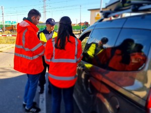 Zdjęcie przedstawia: 
Umundurowanego policjanta rozmawiającego z kierowcą oraz dwojgiem pracowników Kolei Śląskich. Samochód znajduje się przed przejazdem kolejowym.