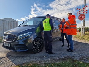 Zdjęcie przedstawia: 
Policjanta rozmawiającego z przedstawicielami Kolei Śląskich oraz kierowcę samochodu.