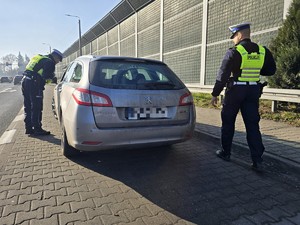 Zdjęcie przedstawia: policjantów podczas kontroli drogowej. Stoją obok pojazdu.