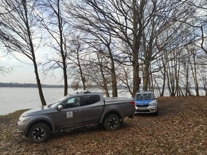 Zdjęcie przedstawia: dwa samochody stojące na brzegu jeziora.