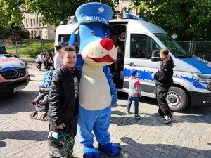 Zdjęcie przedstawia: mężczyznę stojącego z maskotką.