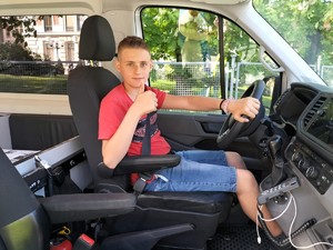 Zdjęcie przedstawia: chłopca siedzącego za kierownicą radiowozu.