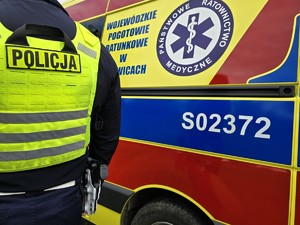 Zdjęcie przedstawia: policjanta i karetkę pogotowia.