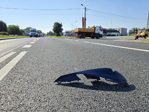 Zdjęcie przedstawia: auto ciężarowe i resztki rozbitego motocyklu, leżące na drodze.