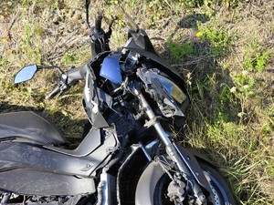 Zdjęcie przedstawia: zniszczony przód motoru, który leży na trawie.