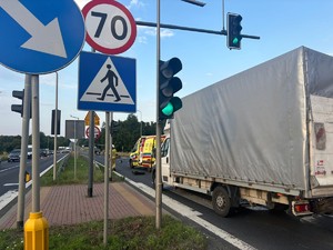 Zdjęcie przedstawia: karatekę pogotowia i auto dostawcze, które stoją obok sygnalizacji świetlnej.